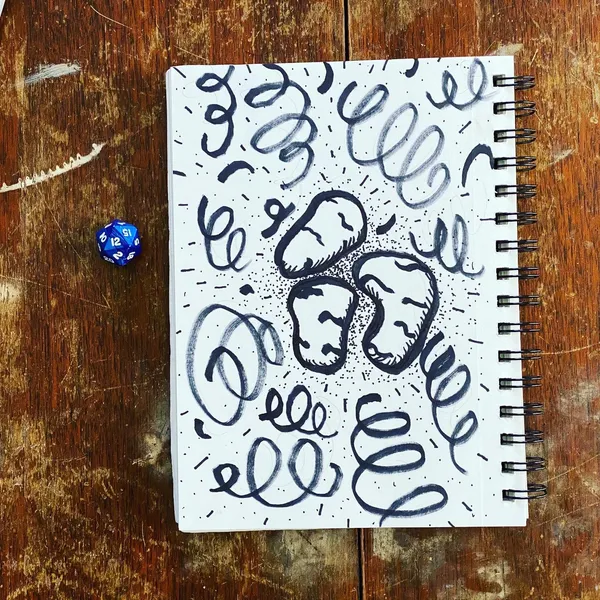 On a rustic wooden surface, a spiral notebook displays black ink drawings of looping spirals and a cluster of three stylized shapes, accompanied by two blue dice.