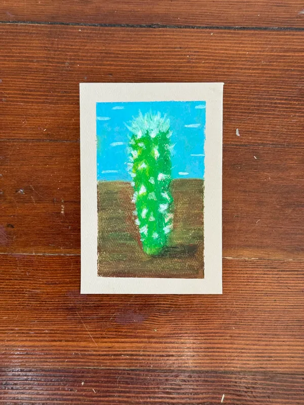 A colorful drawing features a tall, spiky green cactus centered between a bright blue sky and a brown patch of ground, rendered with visible strokes.