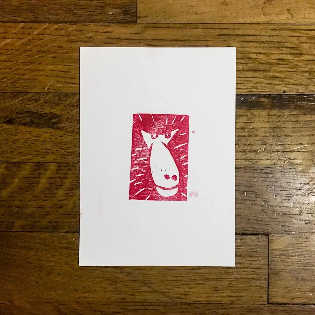 A white card displays a centered red square graphic. The graphic contains a white, stylized, elongated face with two eyes, surrounded by radiating red lines.