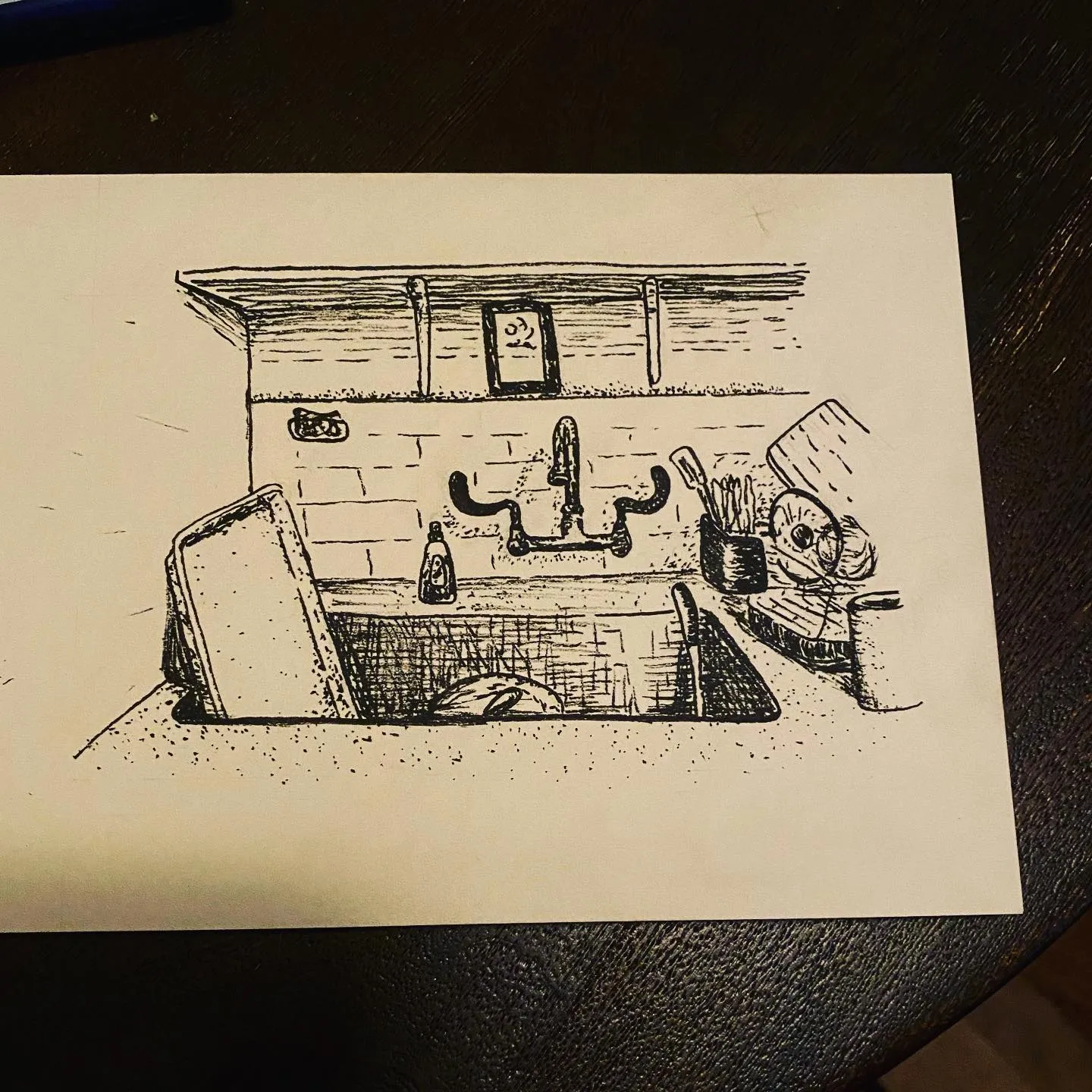 Black ink sketch of a kitchen sink and counter, featuring a faucet, soap dispenser, and various objects sketched across the surface beneath a tiled backsplash.