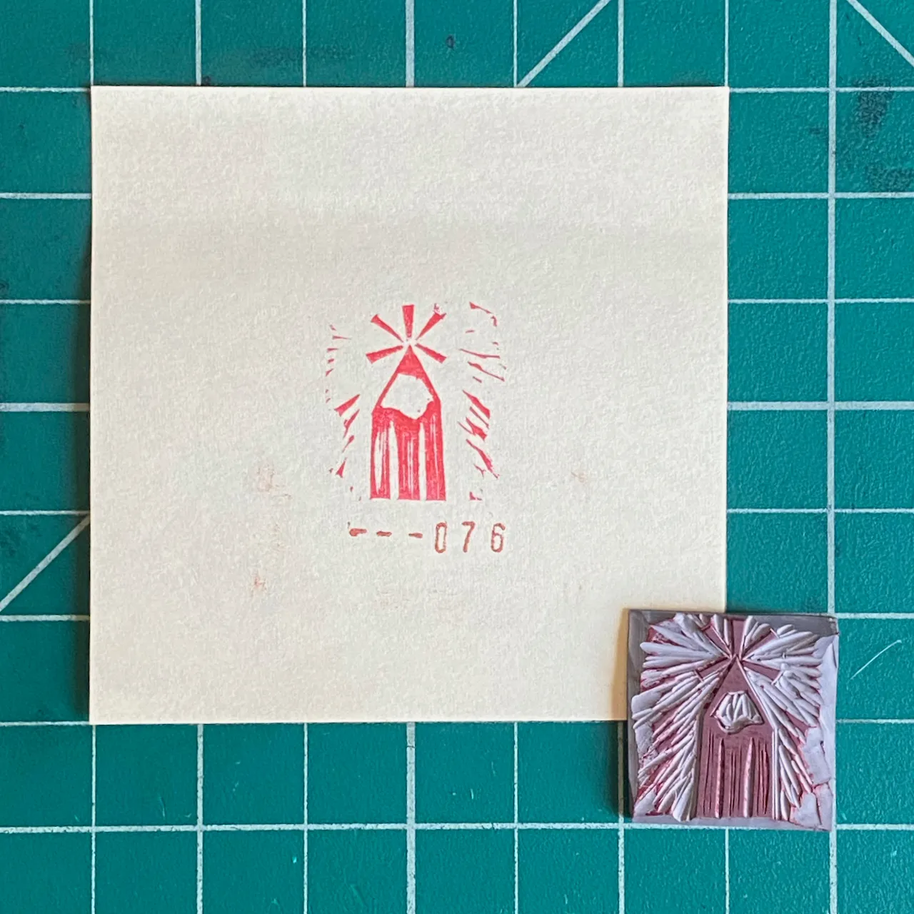 A cream square paper on a teal grid displays a red stylized starburst and the number --076, next to a small, textured pink and white square featuring a similar design.