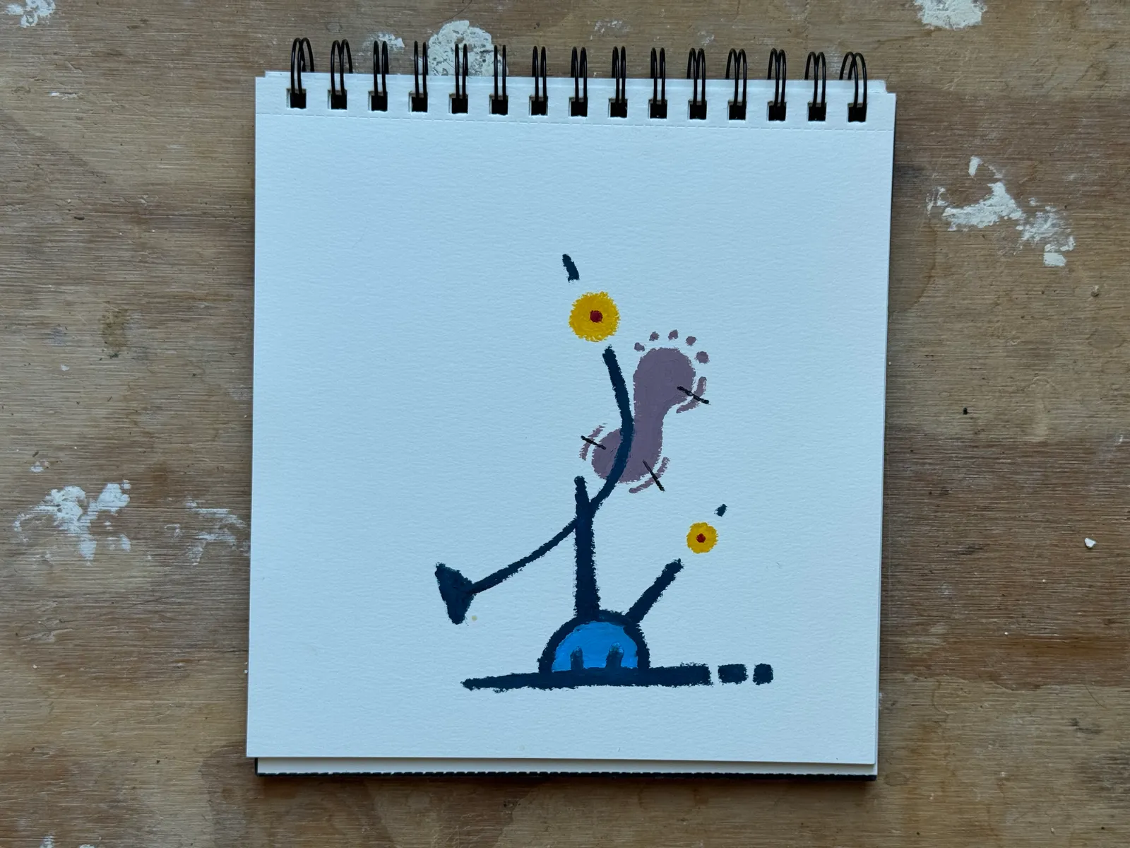 A balancing object with purple and blue tones. The object is balancing on a bright blue base. Small yellow dots decorate the tips of the balancing object.