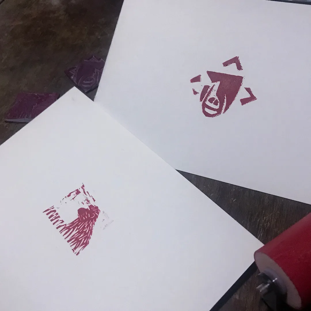 On a dark surface, several white papers display abstract reddish-pink marks, including a geometric figure on the top right and clustered vertical lines on the bottom left.