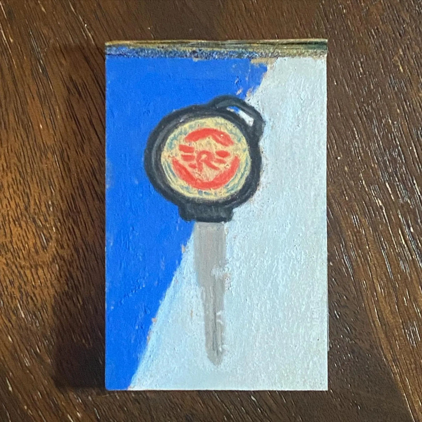 A stylized key hangs from a black-bordered circular badge featuring a red emblem, positioned over a background divided diagonally by deep blue and white paint.