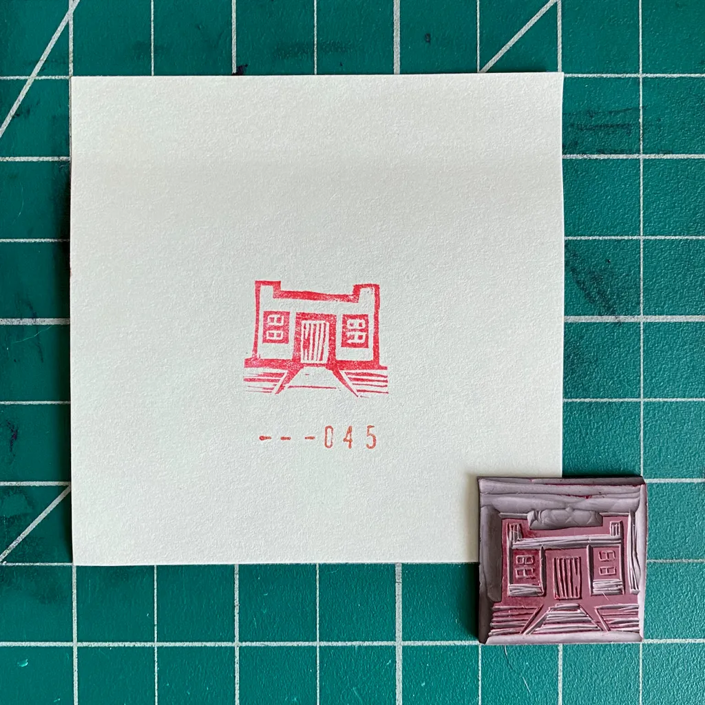 A white square on a green grid features a red drawing of a symmetrical building facade and the numbers 045, positioned above a small, textured pink and white square depicting a similar structure.