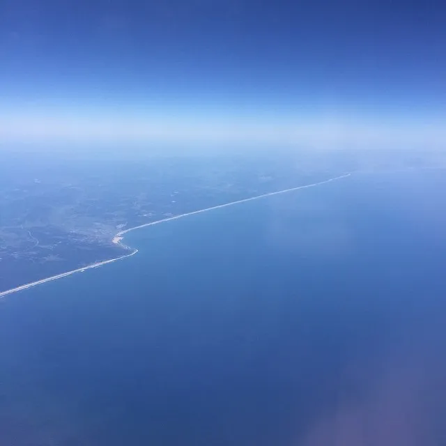 Deep blue ocean meets a hazy blue sky at the horizon, with a curved, lighter coastline visible in the lower left quadrant.