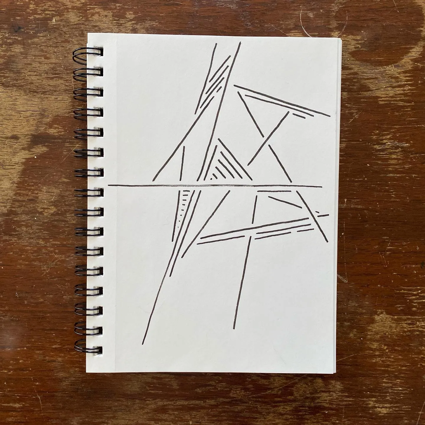 Black ink lines sketch an abstract, angular structure on white paper, depicting intersecting planes and supports divided into two sections by a horizontal line.