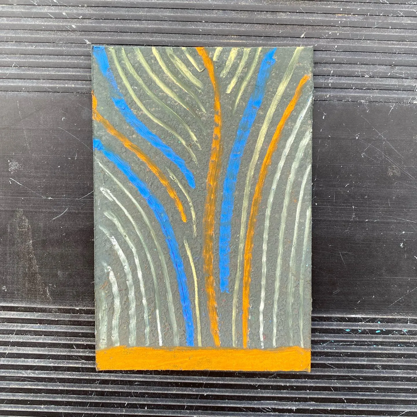 A vertical abstract painting features a gray background with wavy blue and orange lines, grounded by a solid orange horizontal band.
