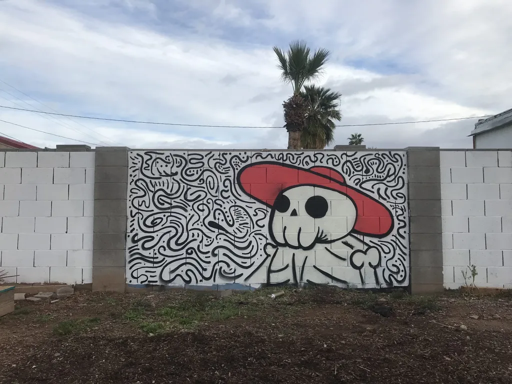 A mural painted on a white wall features a stylized skull wearing a red hat, surrounded by intricate black and white swirling abstract patterns.