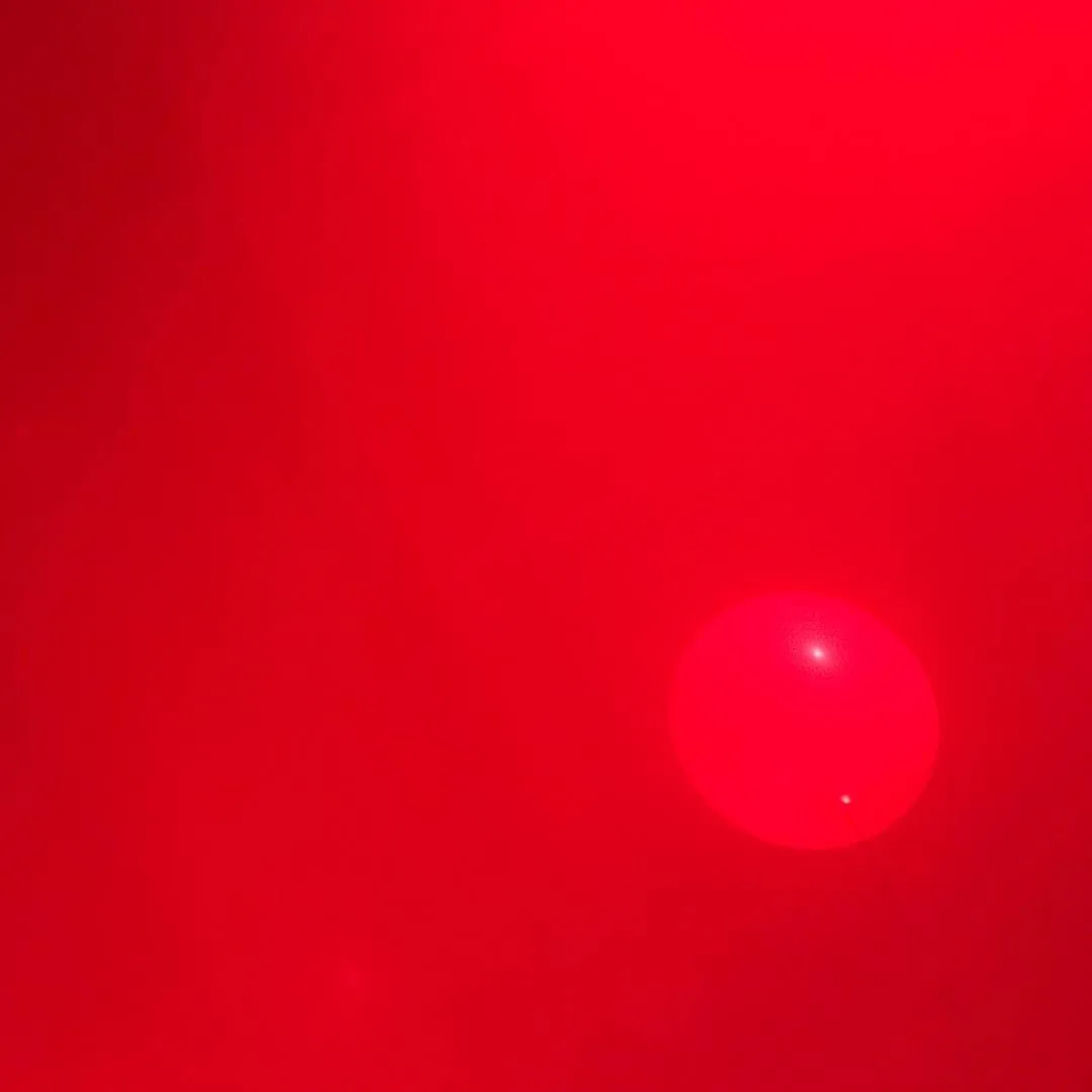 A vibrant red field dominates the composition, featuring a smooth, glowing red circle positioned in the lower right quadrant.