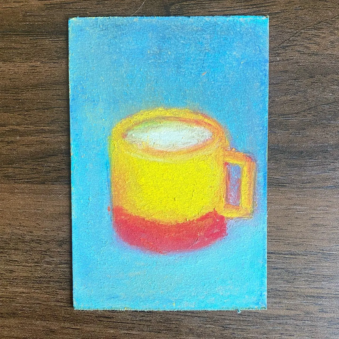 A centered drawing depicts a yellow mug with a red base and white interior, set against a solid bright blue background.