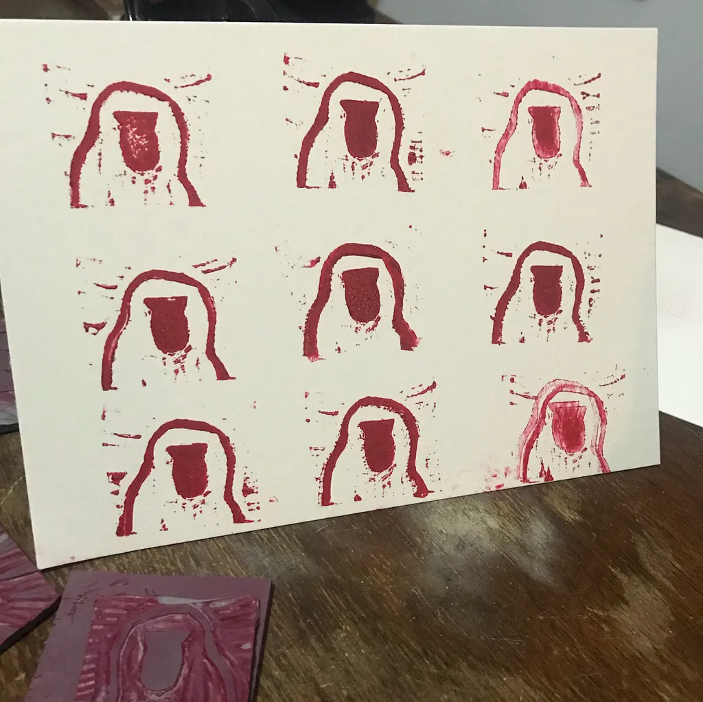 Nine repeating reddish-pink abstract head shapes are arranged in three rows of three on a white surface, showing pigment bleeding and smudging around the edges.