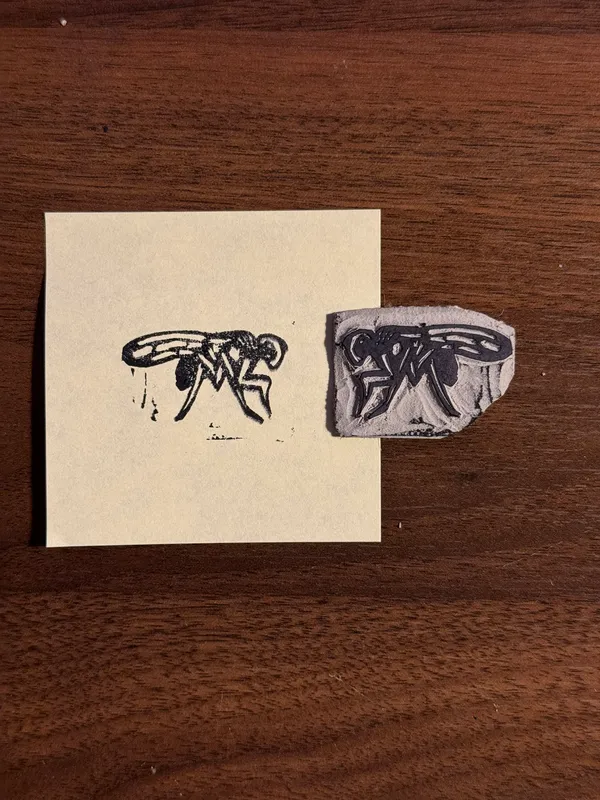 Two stylized black ink drawings of insects are displayed on a dark wood background, with one drawing on a light cream square and the second on a textured gray piece.