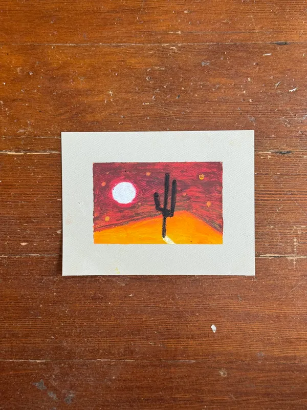 A small, square painting depicts a desert scene with a black saguaro cactus silhouetted against a yellow-orange ground and a deep red sky featuring a white circle.