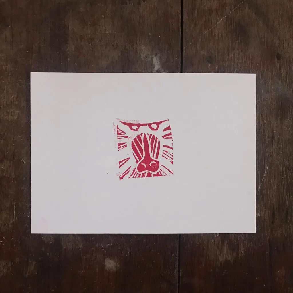 A square drawing of a stylized face, rendered in red and pink geometric lines, is centered on a white card placed on dark wood.