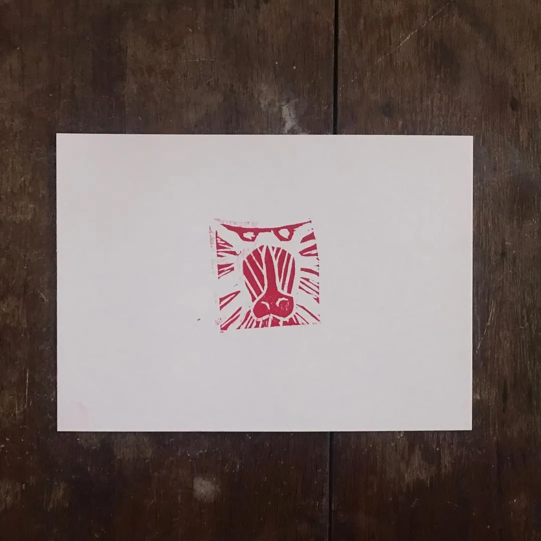A square drawing of a stylized face, rendered in red and pink geometric lines, is centered on a white card placed on dark wood.