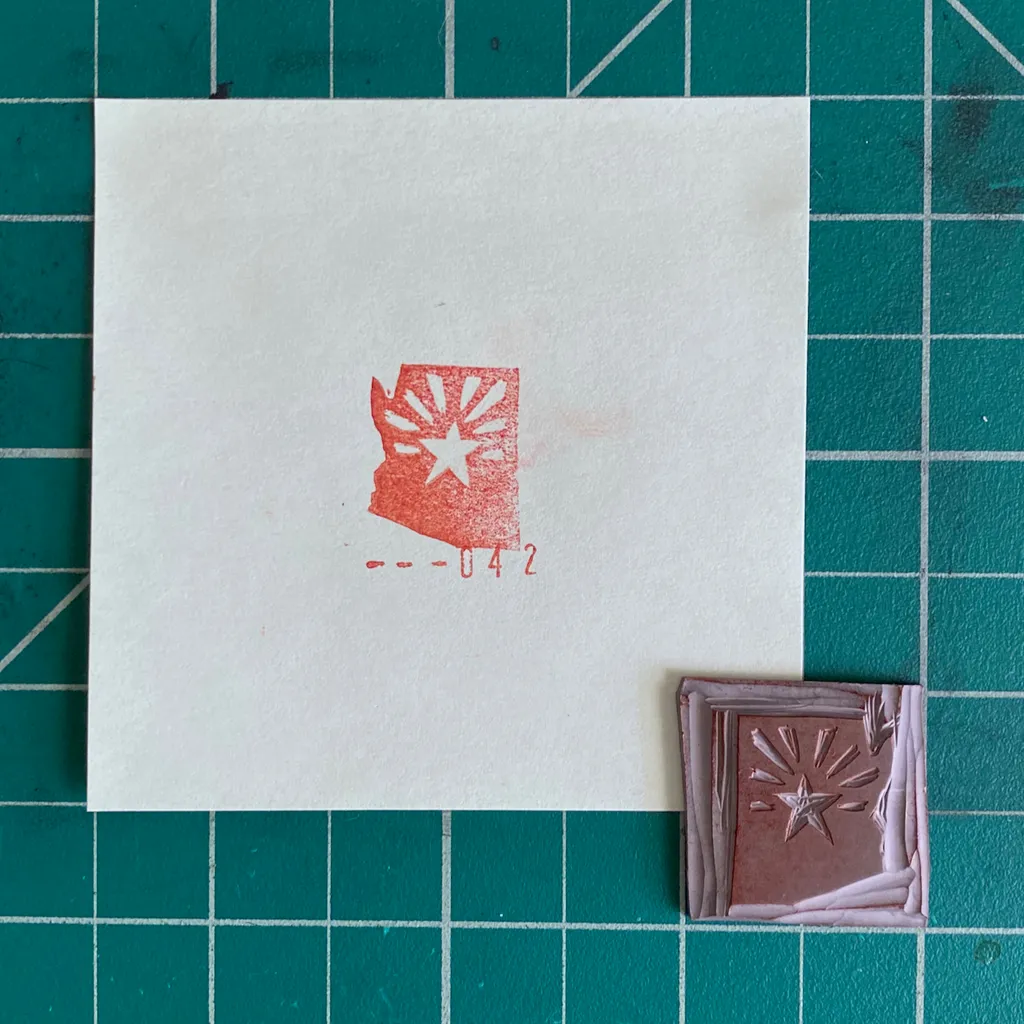 On a teal grid, a white card features a reddish map of Washington State with a starburst and the number --042, positioned above two small reddish-brown rectangles displaying star motifs.