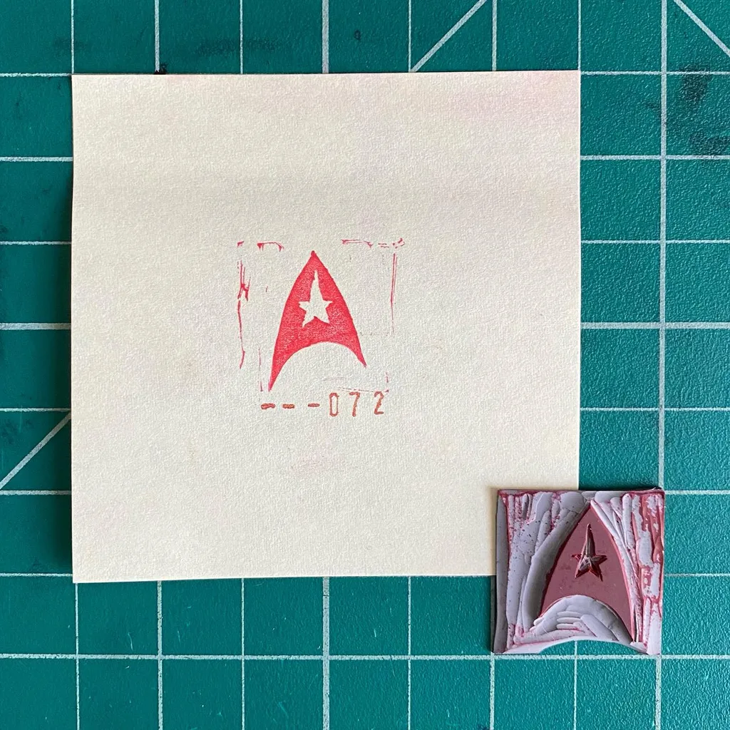 The composition features a large cream paper displaying a red compass rose and the numbers -072, alongside a smaller, layered piece with a red star and compass design.