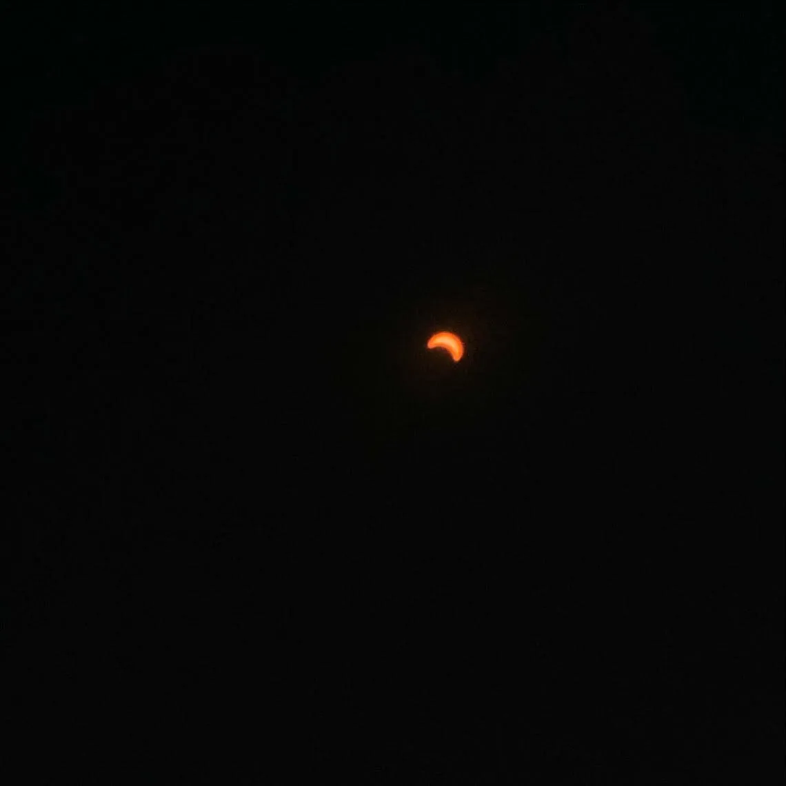 A reddish-orange crescent is centered against a deep, uniform black background.