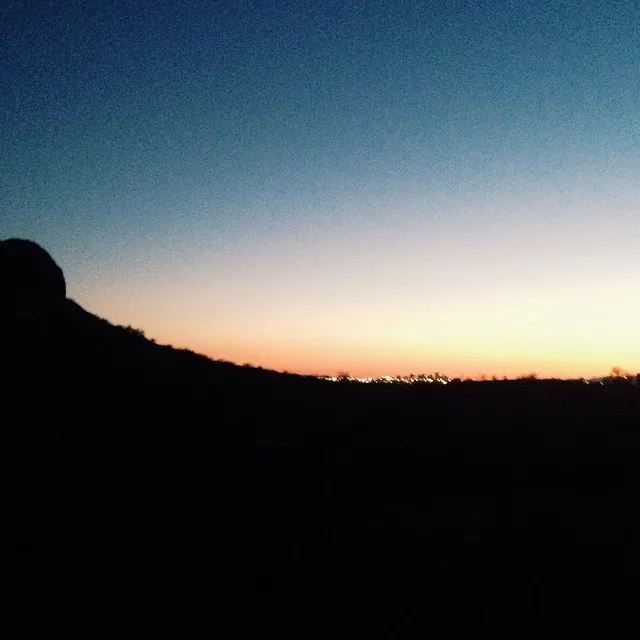 A gradient sky transitions from deep blue at the top to soft yellow and orange near the horizon, silhouetting a dark, rolling landscape below.