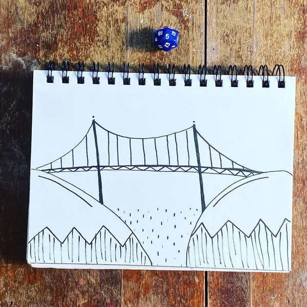 A black line drawing of a suspension bridge spanning between two hills is on a white notepad, which rests on a textured wooden surface near two visible dice.