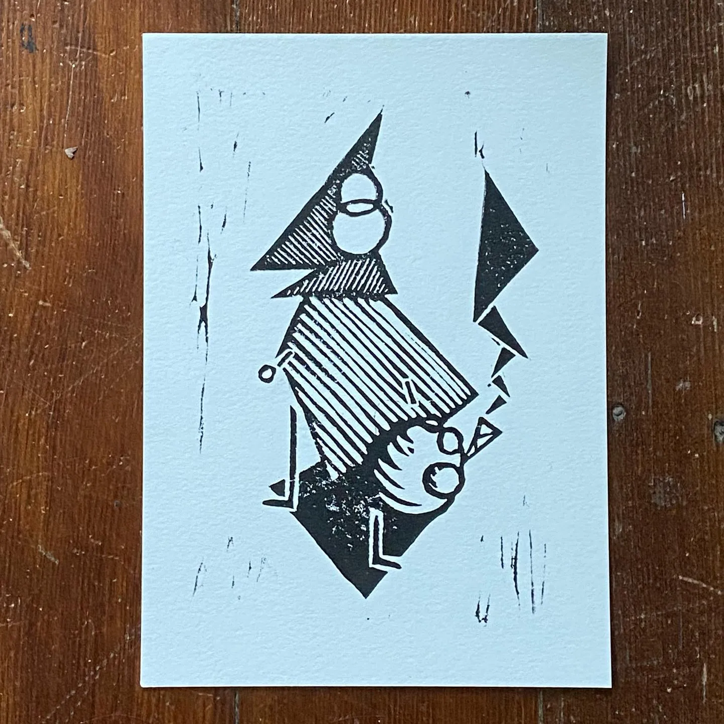 A black ink drawing on white paper features a geometric figure with a pointed head and striped torso, positioned next to a large, sharp black triangle.
