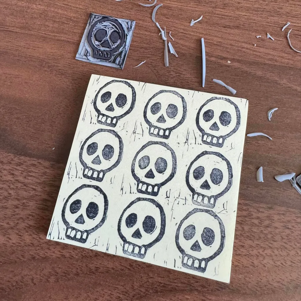 A sheet of yellow paper featuring twelve repeating black outline drawings of stylized skulls is placed on a wooden surface with scattered paper scraps.