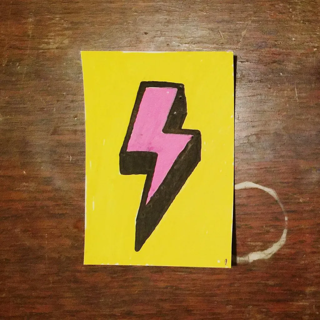 A yellow square contains a stylized lightning bolt drawn in black and filled with bright pink, placed on a dark wooden surface.