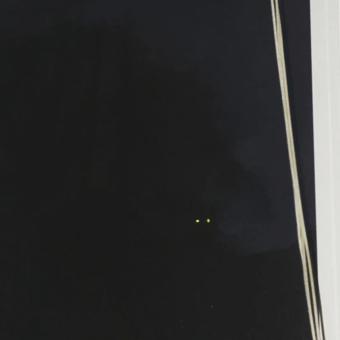 A dark, reflective surface featuring two small yellow-green dots in the lower center and several thin, vertical light lines running along the right edge.