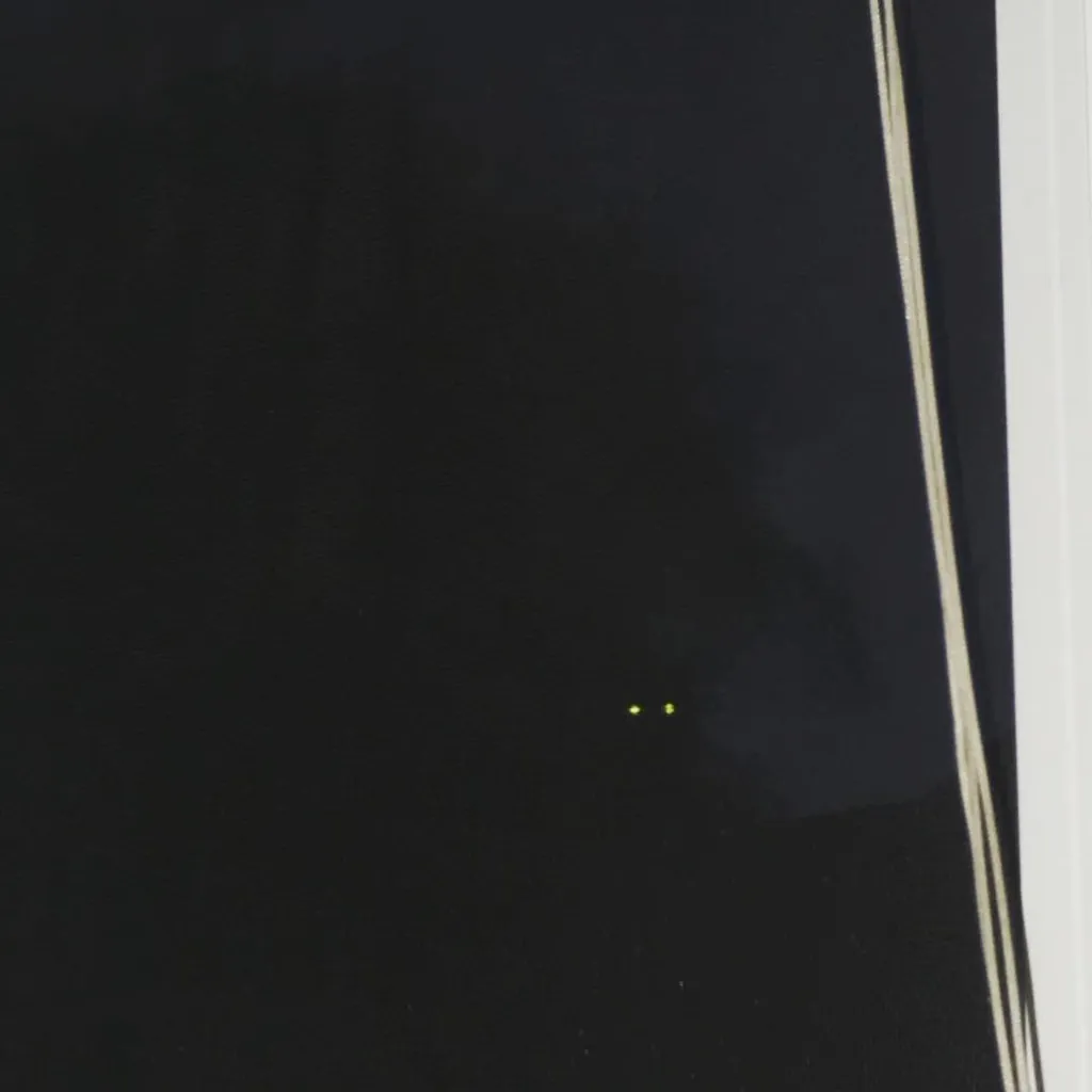 A dark, reflective surface featuring two small yellow-green dots in the lower center and several thin, vertical light lines running along the right edge.