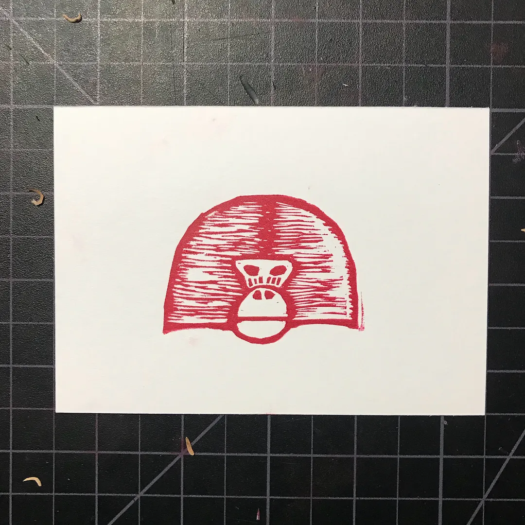 A stylized red drawing of a primate head is centered on white paper, composed of thick, horizontal scribbled lines, with simple lines defining the eyes and muzzle.