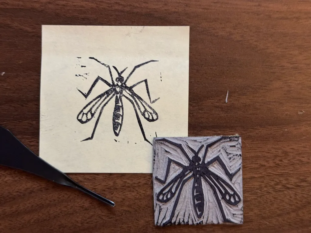 A black ink drawing of an insect on a cream sheet of paper is paired with a second, cross-hatched drawing of an insect on a small, textured gray square, set on a dark wooden surface.