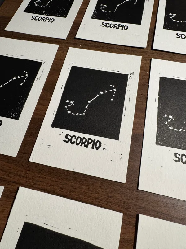 A grid of off-white rectangular cards displays black text and stylized star constellations, with the word SCORPIO printed across multiple visible prints.