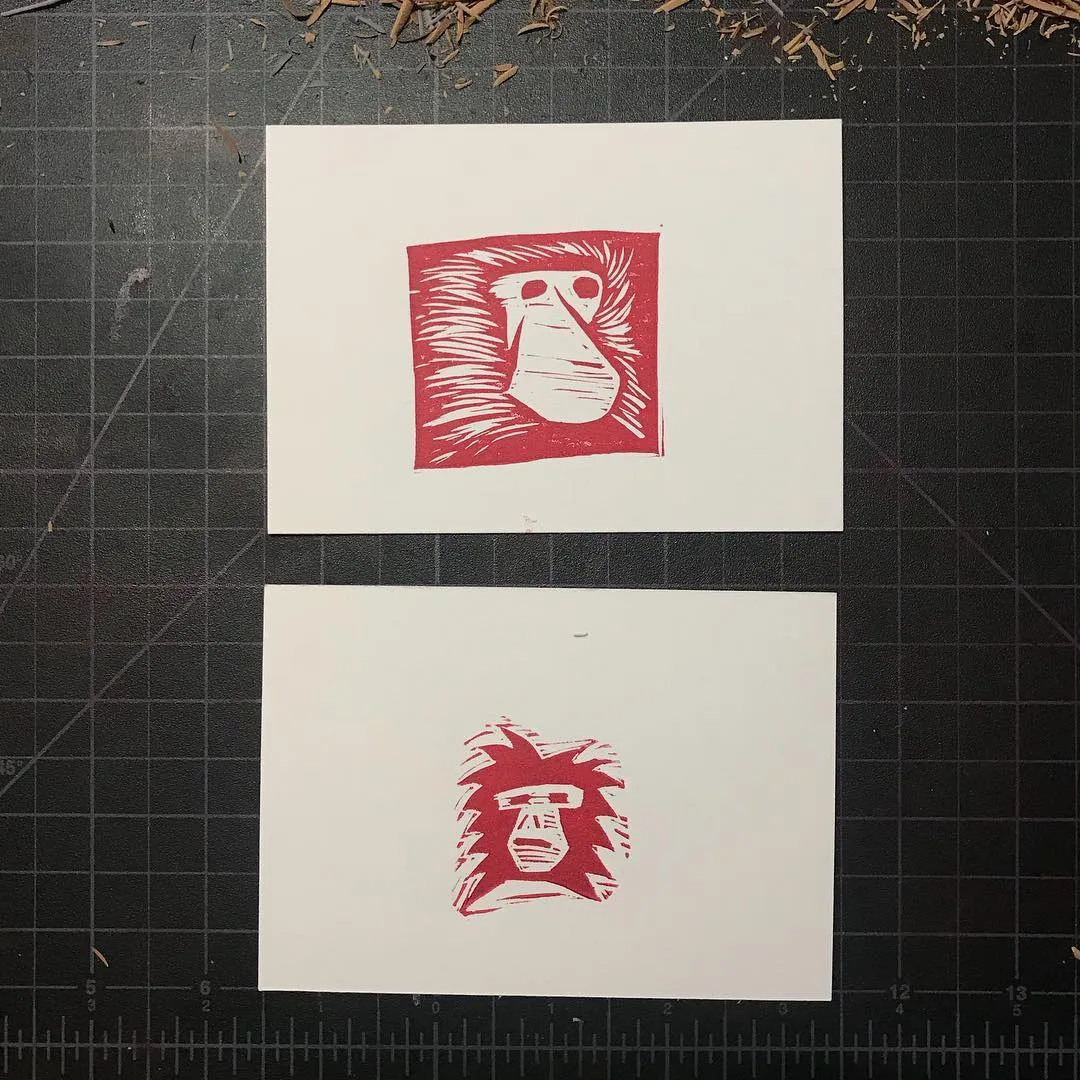 Two stylized red depictions of faces, surrounded by abstract red marks, are displayed on two separate white papers against a dark grid background.
