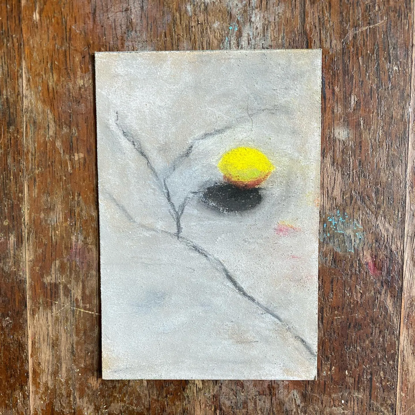 The painting features soft grays and whites, centered on a bright yellow circle connected by dark, branching lines to a dark shape, set against a rustic wooden background.