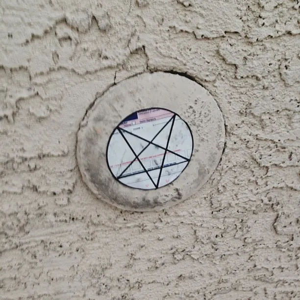 A circular plaque embedded in a textured, light beige wall features a black geometric diagram of intersecting lines forming triangles, along with faint dark text and numbers.