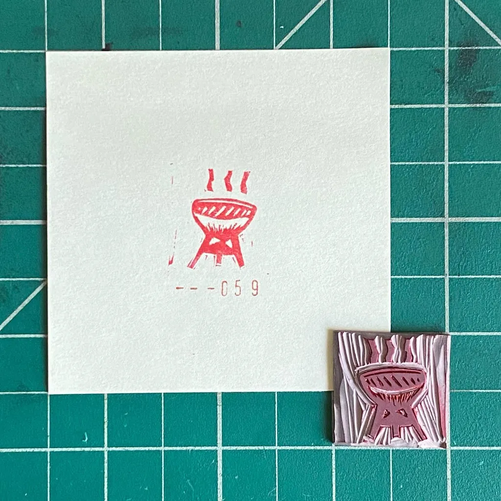A white paper features a red drawing of a stove and the numbers 059, positioned next to a small, textured pink square with a raised, stylized grill design, all on a teal grid background.
