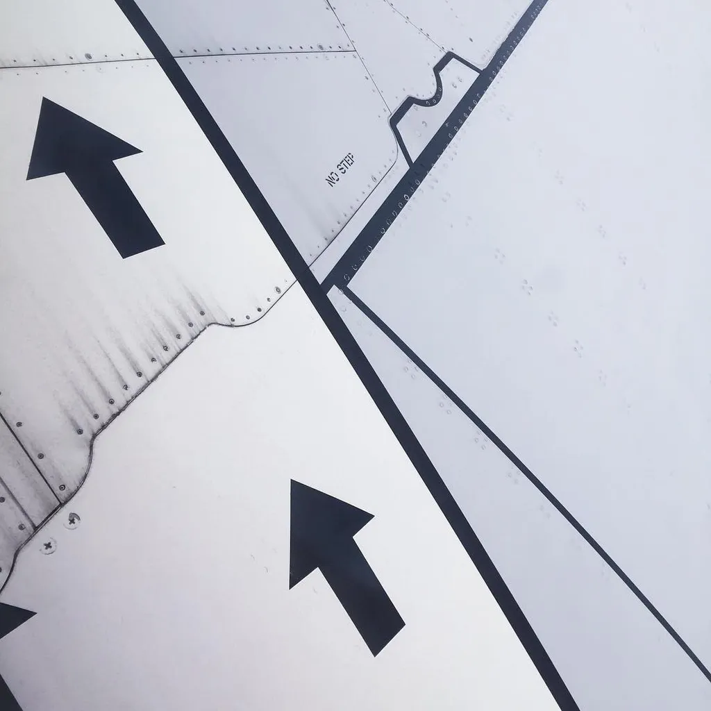 A close-up view of a light gray surface marked with thick black painted lines, including two large directional arrows pointing up and left, and smaller painted text and curves.