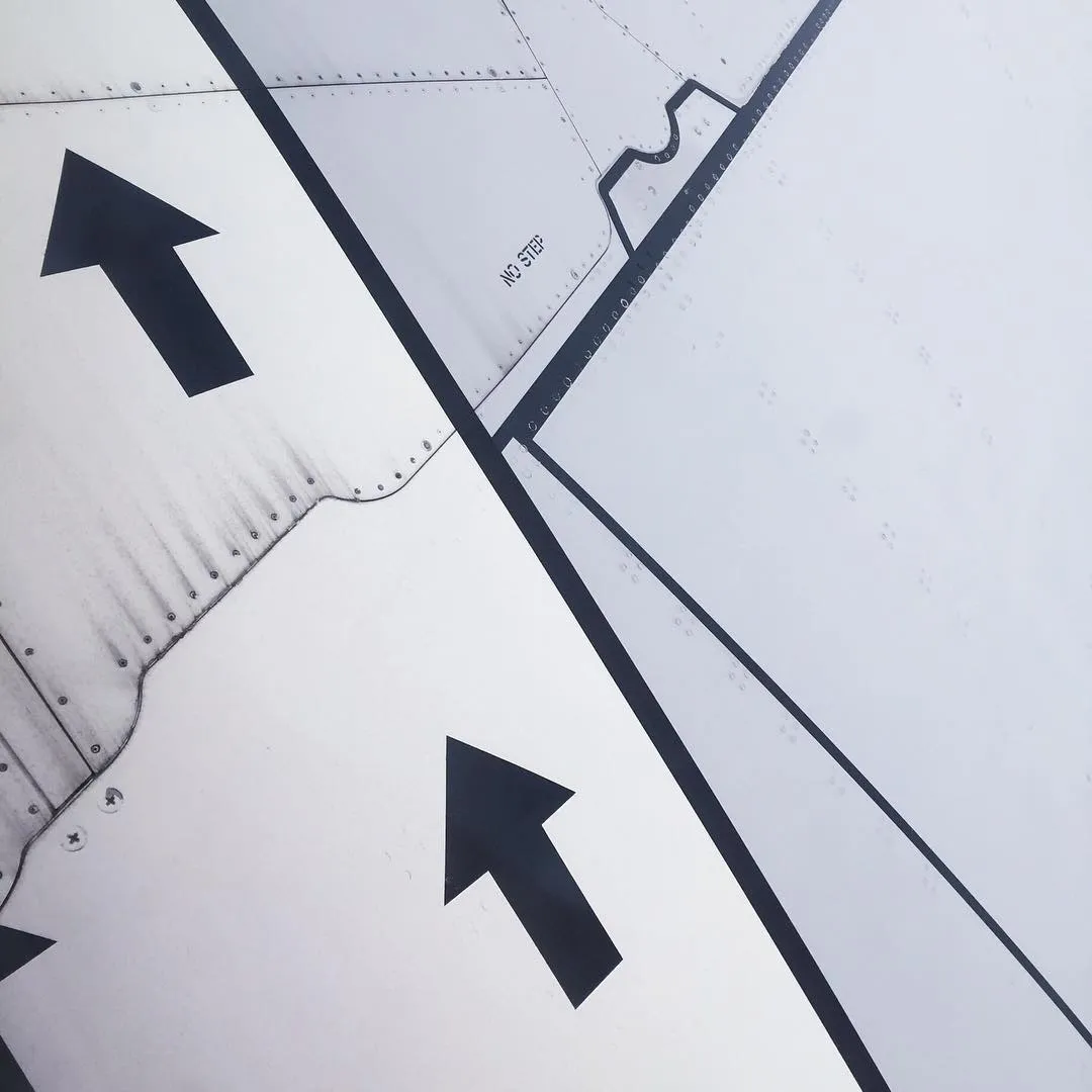 A close-up view of a light gray surface marked with thick black painted lines, including two large directional arrows pointing up and left, and smaller painted text and curves.