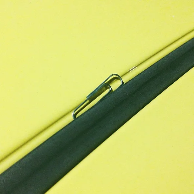 A smooth, dark charcoal strip crosses a vibrant yellow surface, holding a curved, reflective silver clip near its center.