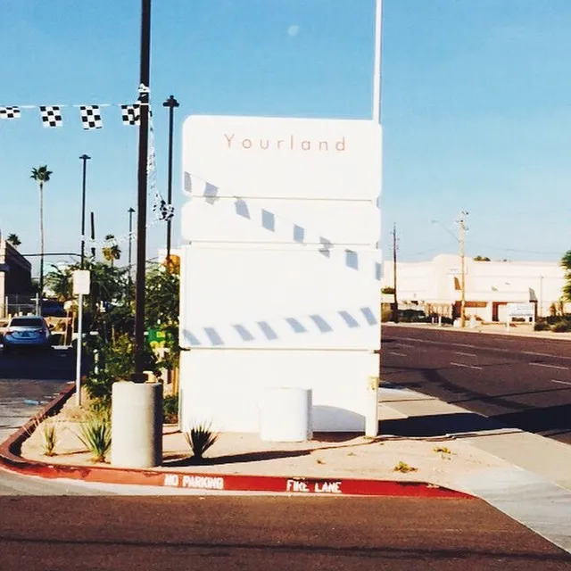 A large white rectangular sign displaying Yourland is decorated with black and white checkered and diagonal striped patterns, situated on a street with visible curb markings.