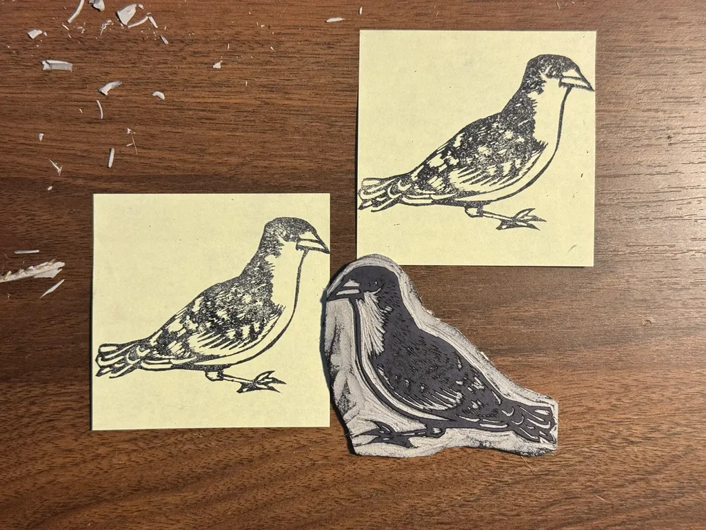 Four black and white drawings of small birds are arranged on a wooden surface scattered with splinters, featuring three birds on small rectangular papers and one larger bird drawing in the foreground.
