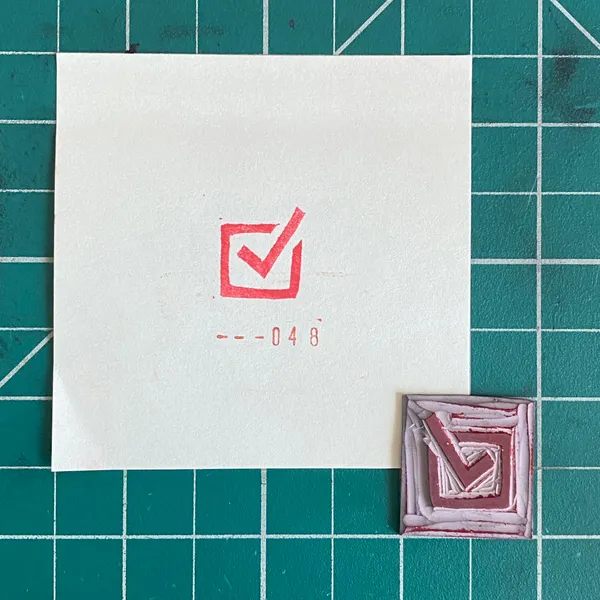 A white square on a teal grid features a red checkmark and the number --048, next to a small, textured square with geometric pink and white lines.