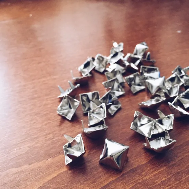 Scattered shiny, crumpled silver pieces rest on a warm brown wooden surface, contrasting the reflective, angular shapes with the visible wood grain.