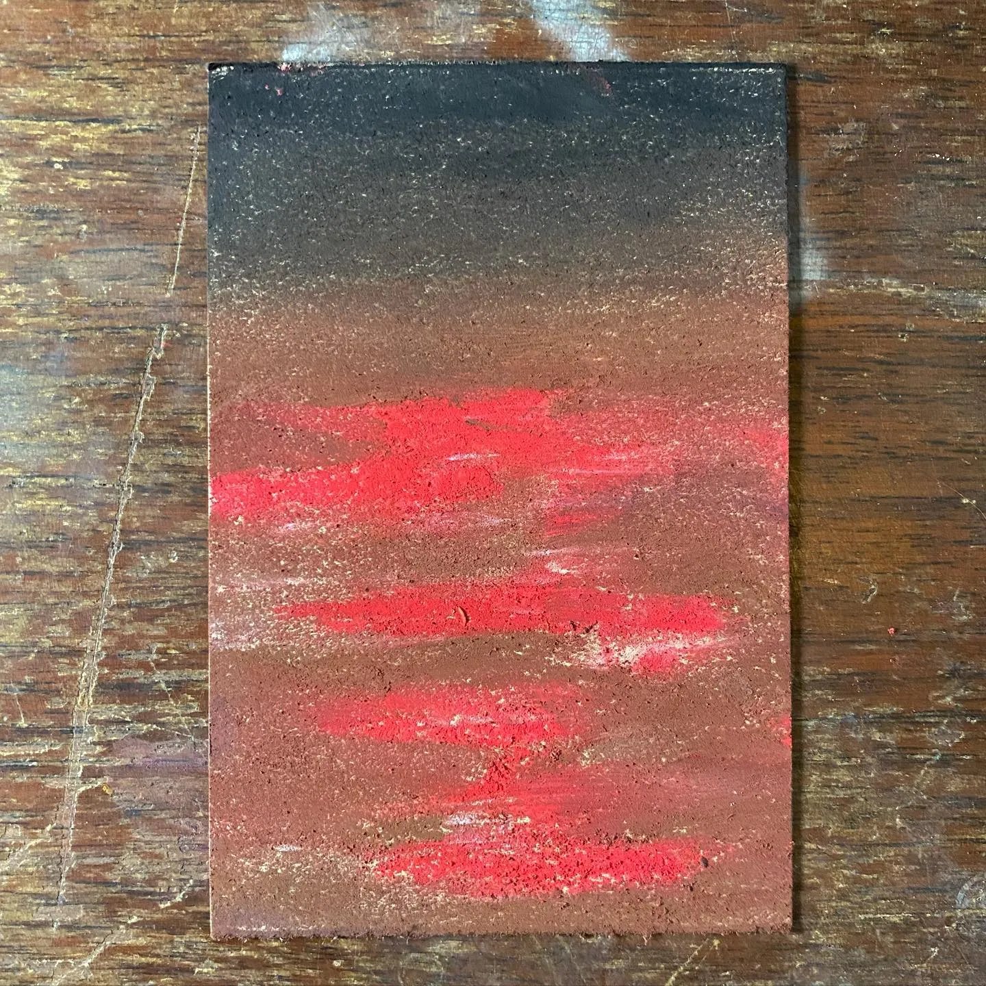 A vertical rectangular artwork features a dark top section that transitions into a reddish-brown bottom section, marked by horizontal streaks of bright red and deep red tones.