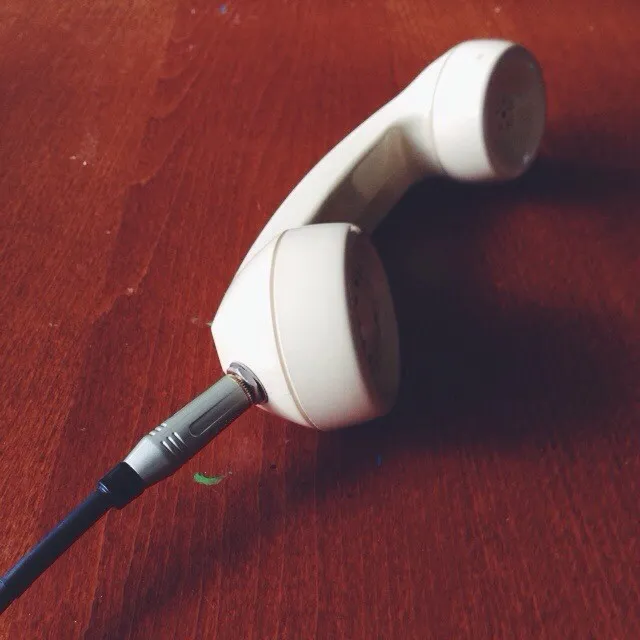A pair of white wired headphones with black tips lies on a reddish-brown wooden surface, showing visible wood grain and strong shadows.