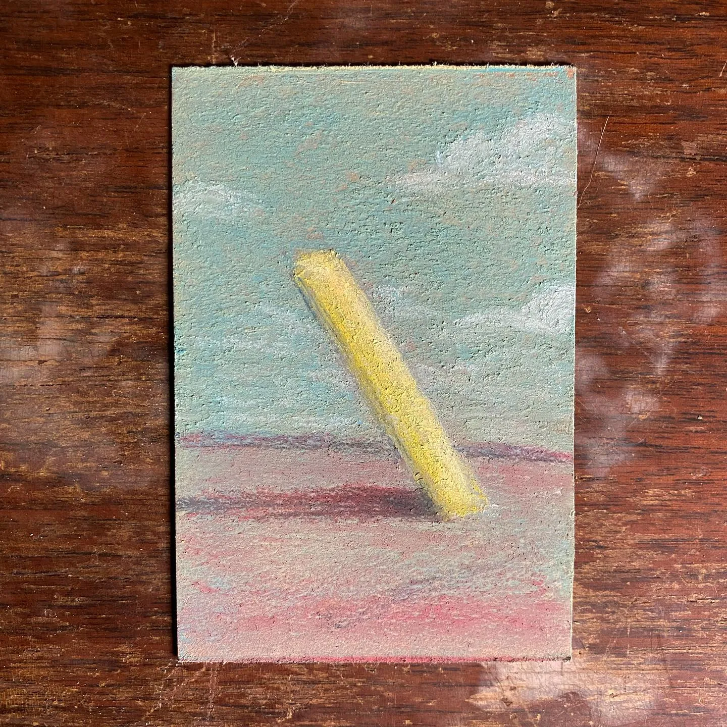 A pale yellow cylinder rests diagonally across a rectangular composition featuring horizontal bands of muted teal, soft pink, and reddish tones.