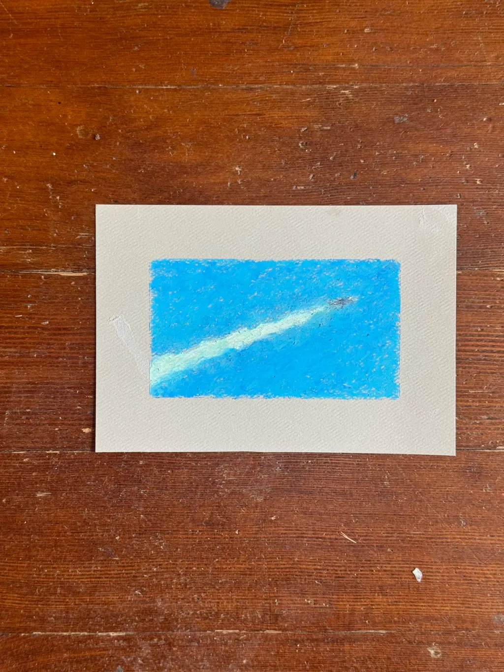 A light blue rectangle on white paper contains a diagonal, streaky white mark, set against a dark brown wooden background.