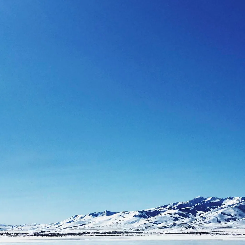Deep blue sky dominates the composition above a low horizon line where snowy, undulating mountains meet a flat, dark foreground.
