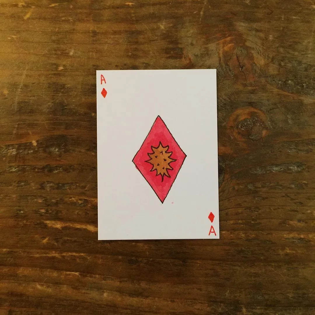 A white card featuring a large red and orange diamond with yellow radiating lines is centered on a dark brown wooden surface showing visible grain.